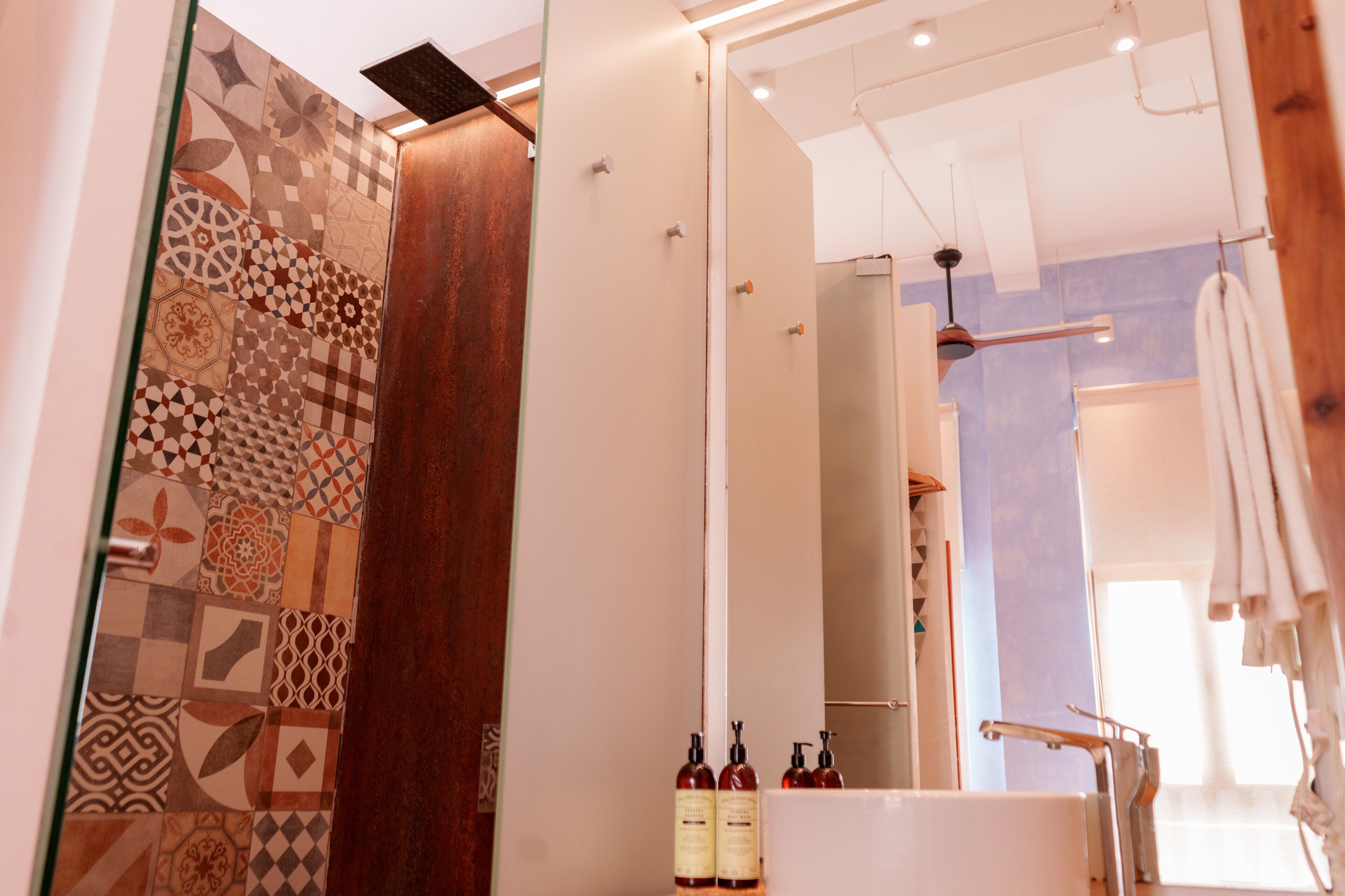 Un baño moderno con baldosas estampadas, una puerta de madera, un lavamanos blanco y un espejo.