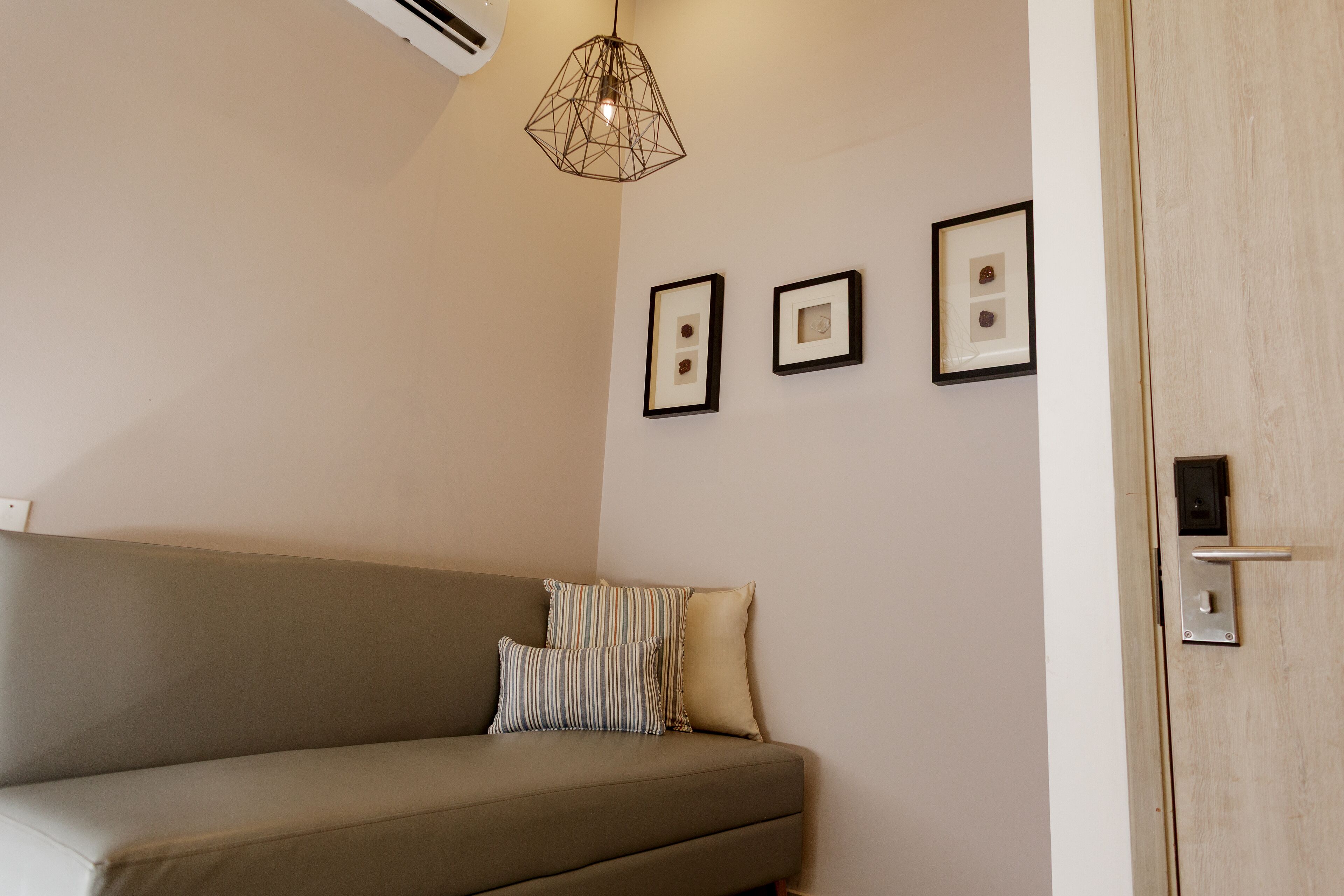 Um quarto em tons neutros, com um sofá bege, uma luminária pendente geométrica e três quadros na parede.