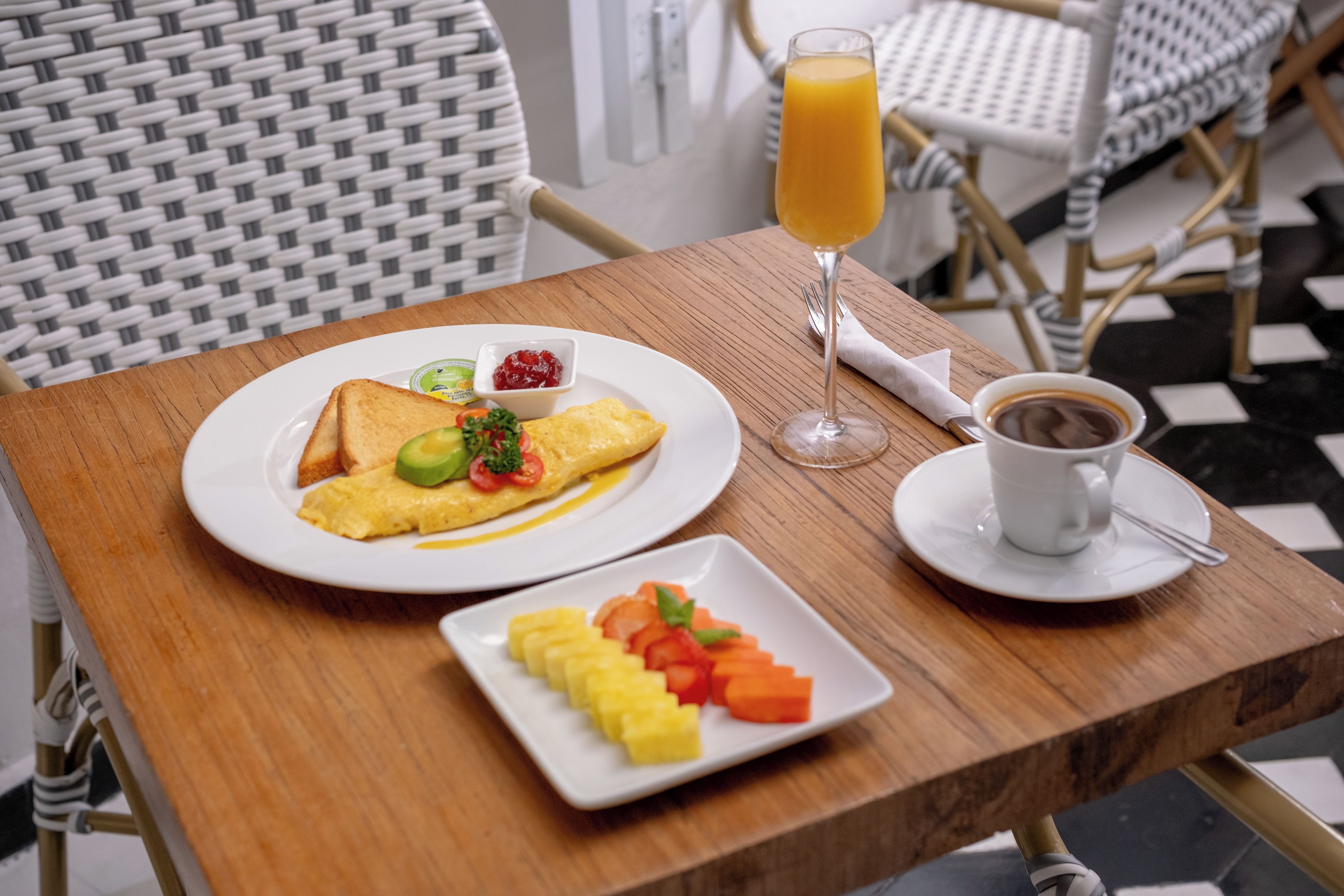 A breakfast setting with toast, omelette, fruit, coffee, and orange juice on a wooden table.