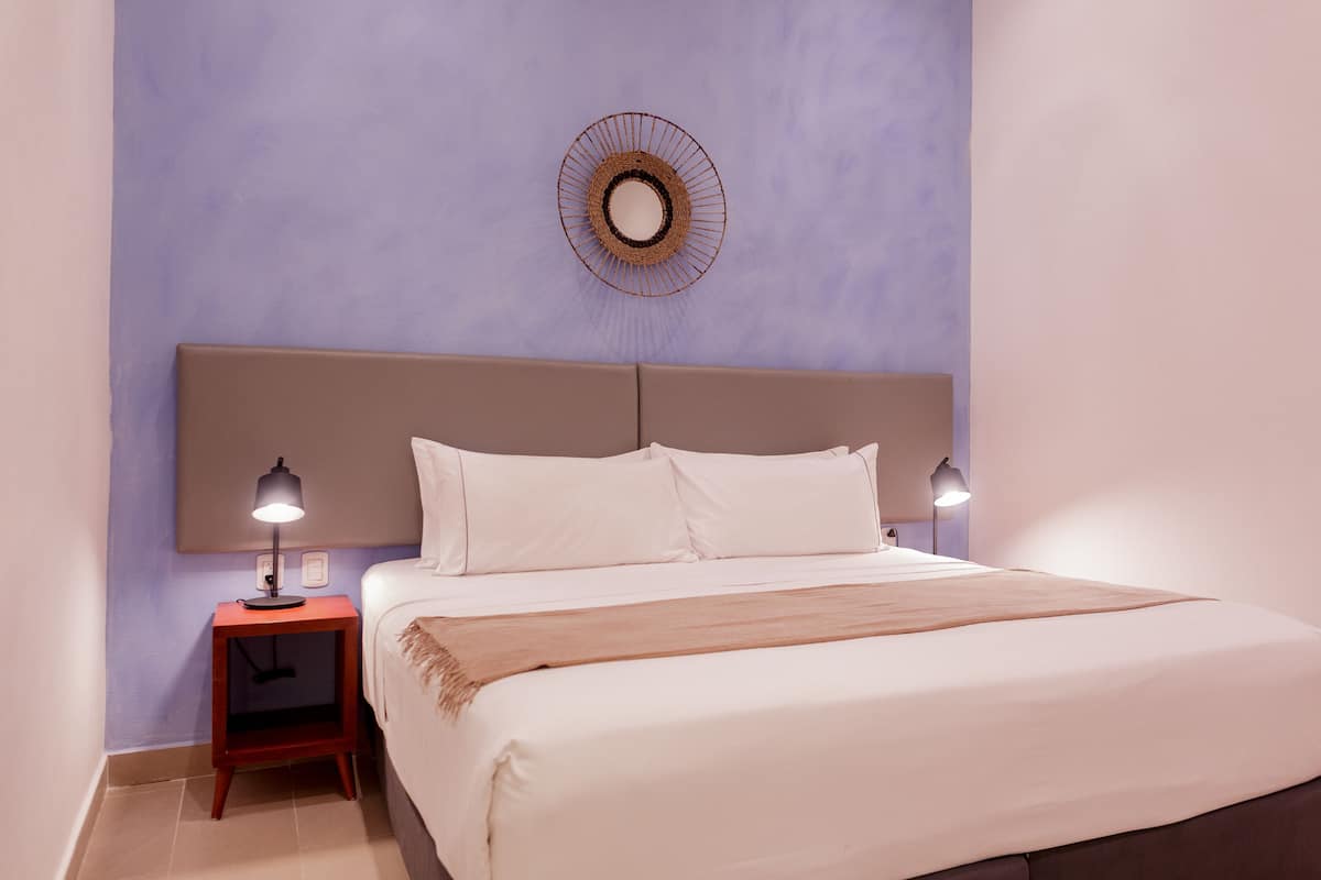 A bedroom with a bed, two bedside tables, a wall-mounted mirror, and a light fixture.