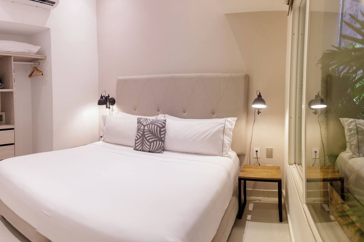 A neatly made bed with a headboard, bedside tables, and a hanging light fixture.