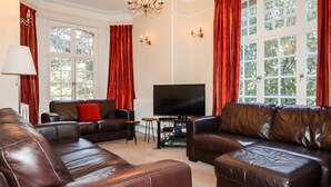A living room with leather sofas, a flat-screen TV, and red curtains. - Lewarne (Boscastle)