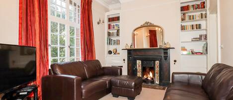 A living room with a fireplace, leather sofas, a bookshelf, and a television.