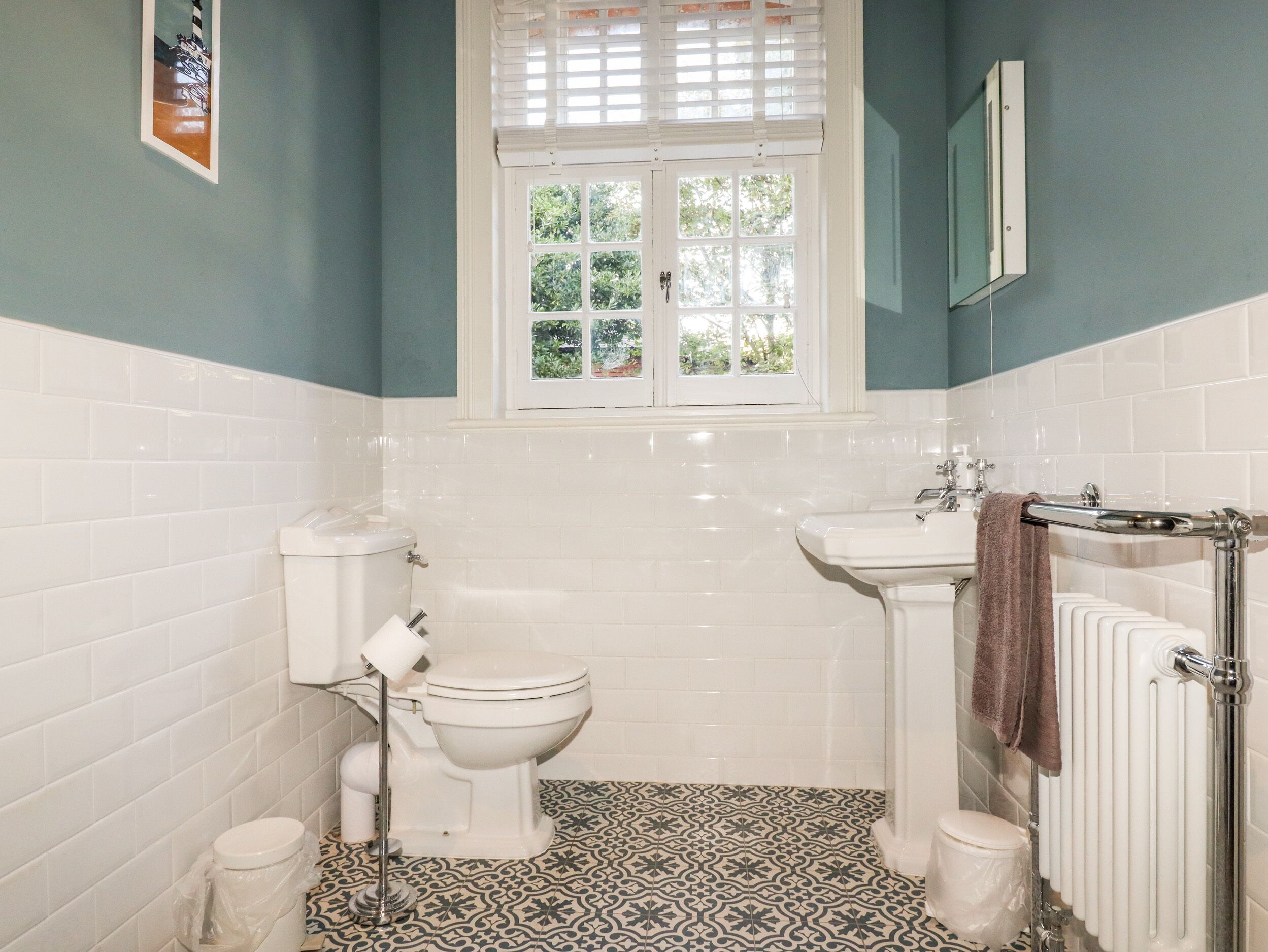 A bathroom with a toilet, bidet, and bathtub, featuring patterned floor tiles and a window with blinds.