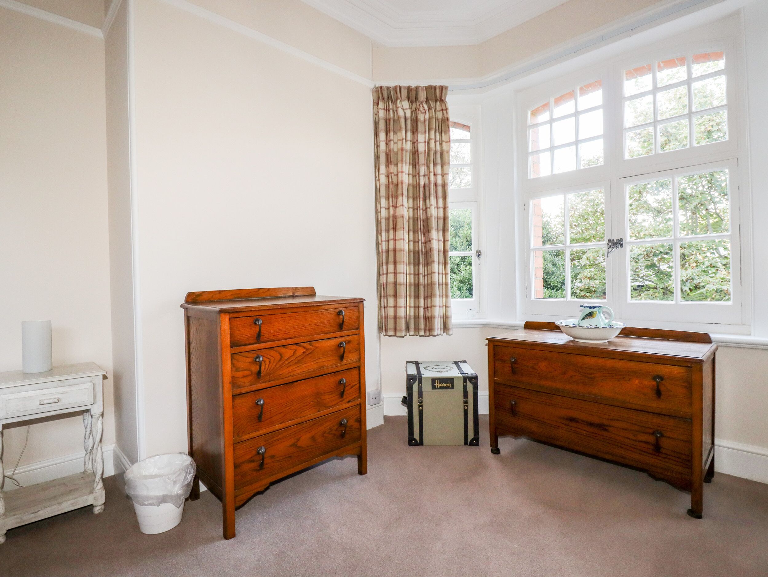 A room with two wooden dressers, a white table, and a window with curtains.