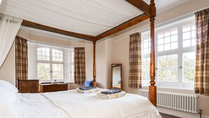 A four-poster bed with a wooden frame, a large window with curtains, a bedside table, and a mirror. - Lewarne (Boscastle)