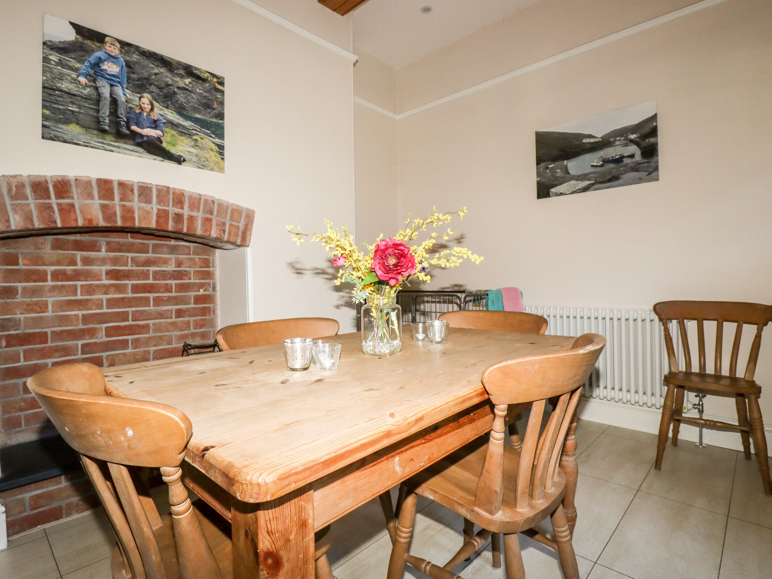 A dining area with a wooden table, four chairs, a vase with flowers, and a brick fireplace.