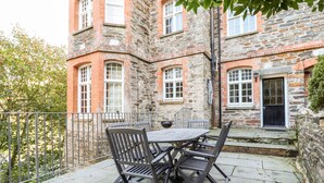 A stone building with a courtyard patio featuring a table and chairs. - Lewarne (Boscastle)