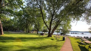 A park with a paved walkway, picnic tables, and benches near a body of water.