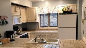 A kitchen with a central island, three stools, a microwave, a stove, a sink, and a refrigerator.