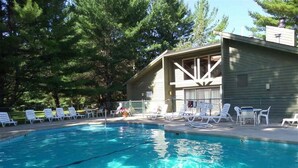 A swimming pool with clear blue water, surrounded by white lounge chairs and a building with a sloped roof.