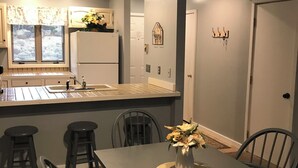 A compact kitchen with a dining area, featuring a central island, a refrigerator, and a window with blinds.