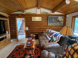 A cozy log cabin interior with a leather sofa, a wooden coffee table, and a patterned rug.