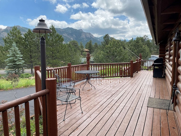A wooden deck with a table and chairs, overlooking a mountainous landscape.