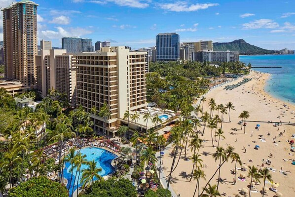 Resort com piscina, praia e edifícios altos ao fundo.