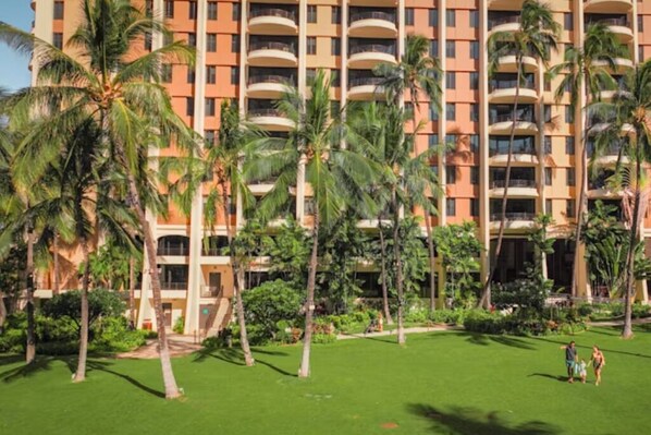 Un hotel de varios pisos con balcones, rodeado de palmeras y un césped bien cuidado.