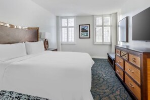 Quarto de hotel com cama, penteadeira, televisão e janela com persianas.