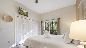 Ein Schlafzimmer mit Bett, Wandfernseher, Fenster mit Vorhängen und einer Tür.