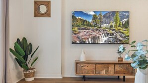 Ein Zimmer mit einem Holzkabinett, einem großen Gemälde einer Berglandschaft, einer Topfpflanze und einem Spiegel an der Wand.
