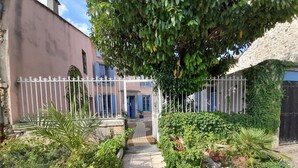 Une entrée fermée par un portail, avec un chemin pavé menant à un bâtiment aux volets bleus.