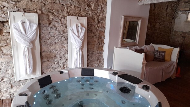 Une salle de spa avec un jacuzzi, deux serviettes accrochées au mur, un lit avec une tête de lit et un mur en pierre.