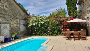 Une piscine dotée d’une terrasse carrelée, entourée d’une végétation luxuriante et de plantes en fleurs.