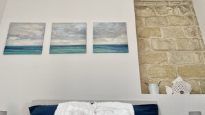 A bedroom with a bed, a stone wall, and three paintings of the sea.