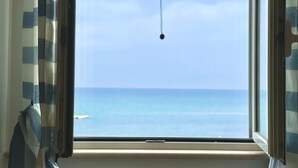 A window with a view of the sea, curtains, and a hanging object.