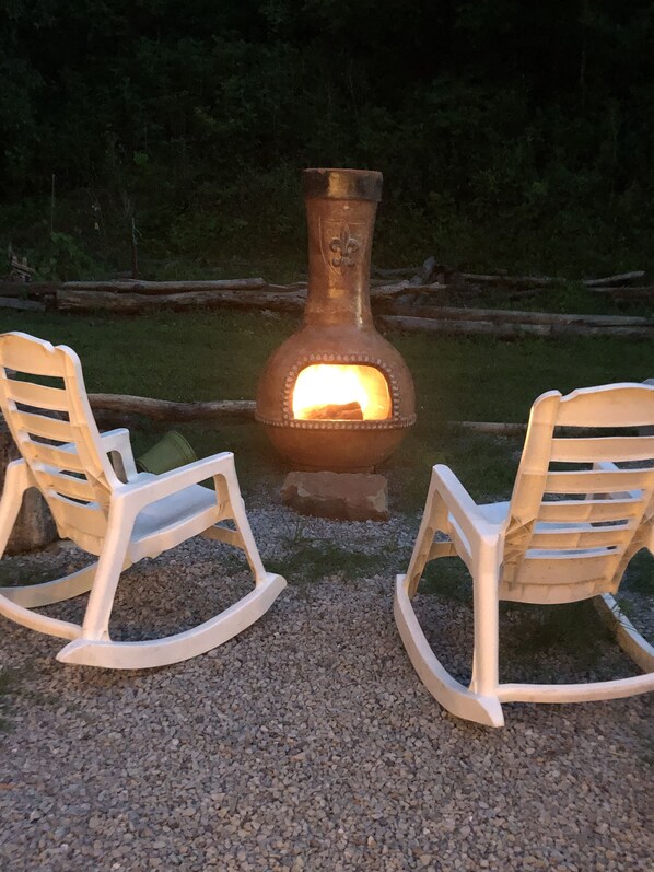 Un espace extérieur rustique aménagé avec deux fauteuils à bascule placés face à un poêle à bois.