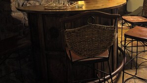 A rustic bar area with stone walls, wooden furniture, and a bookshelf.