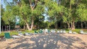 A sandy beach area with green lounge chairs and a playground structure in the background.