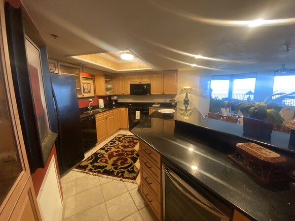 A kitchen with wooden cabinets, a black countertop, a refrigerator, a microwave, and a window with a view of the outside.