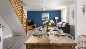 Uma área de jantar com mesa de madeira posta para quatro pessoas, uma televisão e parede azul.