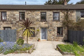 A stone building with a gravel pathway, a door labeled 'Aval Dor Barn,' and a small garden with flowers and a palm-like plant.