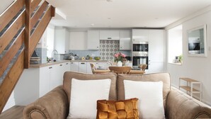 Eine moderne Küche mit weißen Schränken, ein Essbereich mit Holztisch und -stühlen sowie eine Treppe mit Holzhandläufen.
