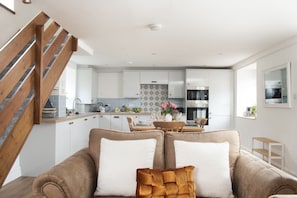 A modern kitchen with white cabinets, a dining area with a wooden table and chairs, and a staircase with wooden railings.