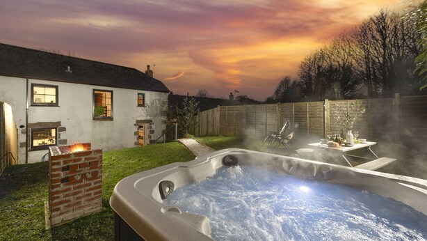 Ein Whirlpool in einem Garten mit einer Ziegelstruktur, einem Holzzaun und einem Haus mit Fenstern.