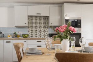 Eine Küche mit weißen Schränken, einer gemusterten Spritzschutzwand und einem Esstisch, der mit Gläsern und Blumen gedeckt ist.