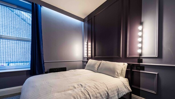 Habitación de hotel con una cama grande, ventana con cortinas e iluminación en la pared.