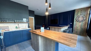 Una cocina moderna con una isla central, armarios oscuros, un televisor montado y un dardo.