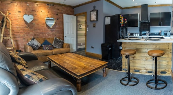 Un salon chaleureux avec un mur en briques, une table basse en bois, un canapé en cuir et un miroir en forme de cœur.