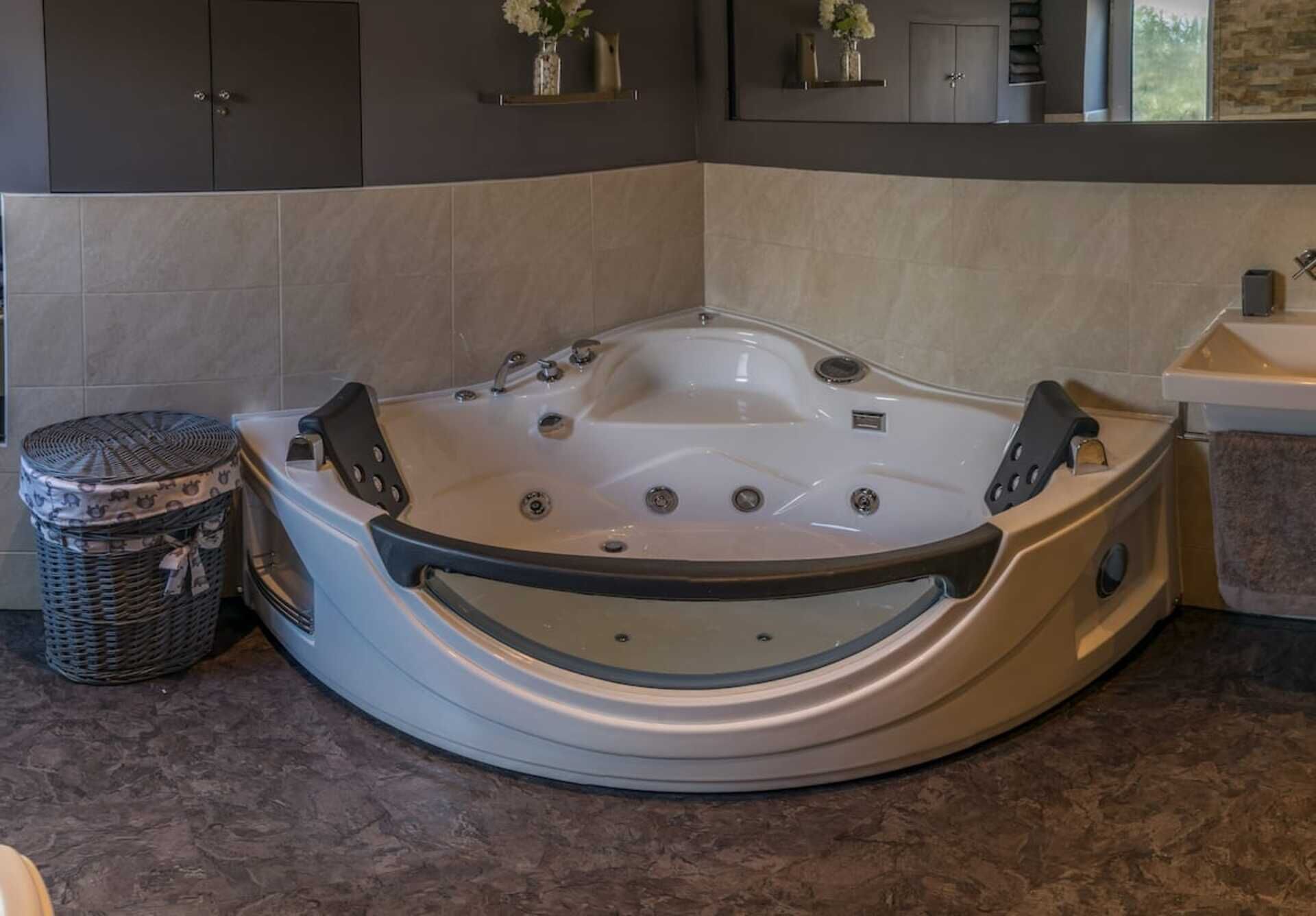 Une salle de bain d’angle avec une baignoire sur pieds, un petit panier en osier et un miroir au-dessus du lavabo.