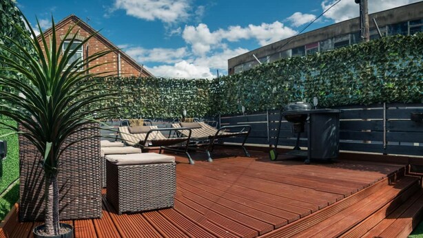 Una terraza de madera con mobiliario exterior, una planta en maceta y una parrilla.
