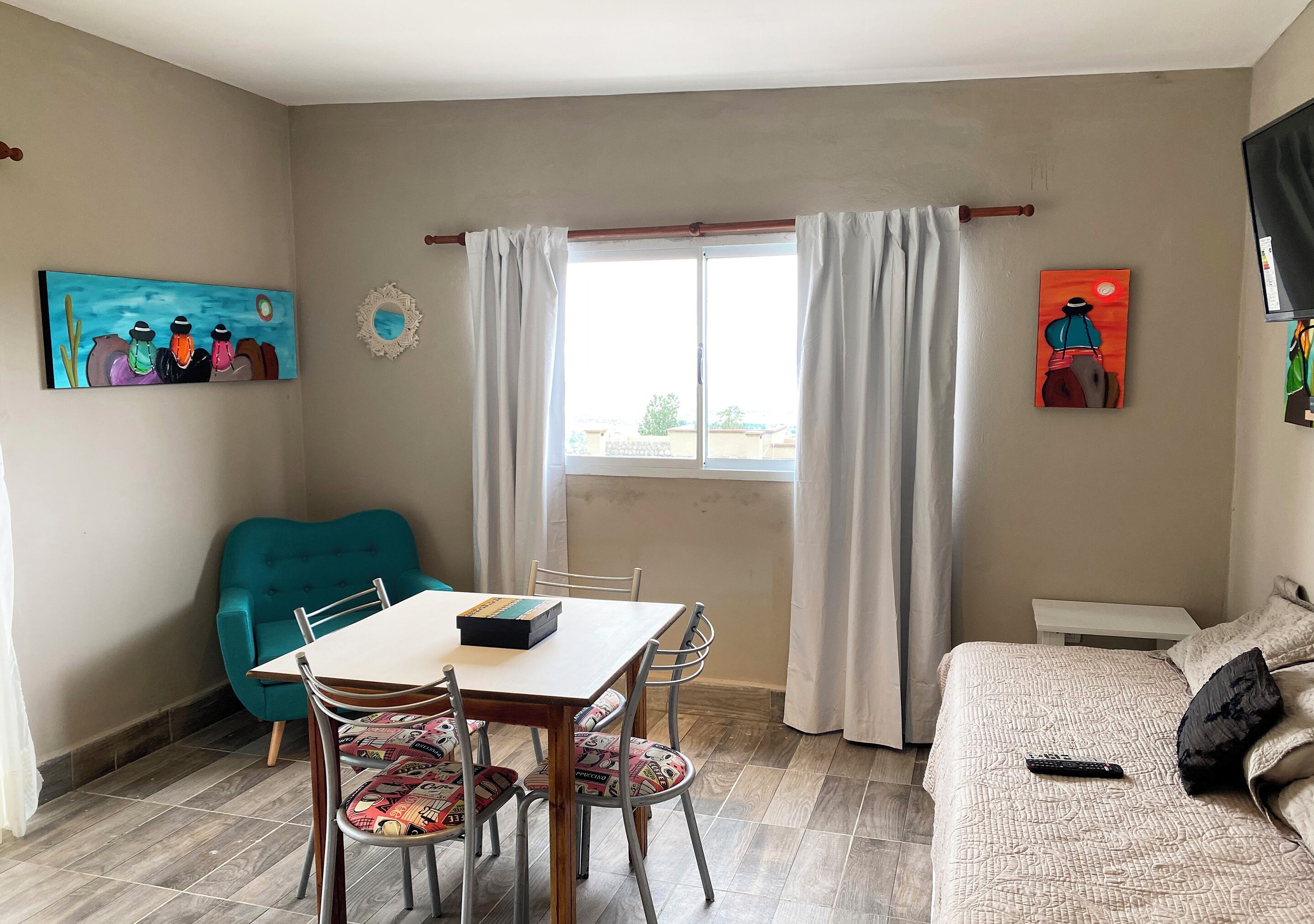 Quarto com mesa de jantar, cadeiras, sofá, televisão e obras de arte nas paredes.