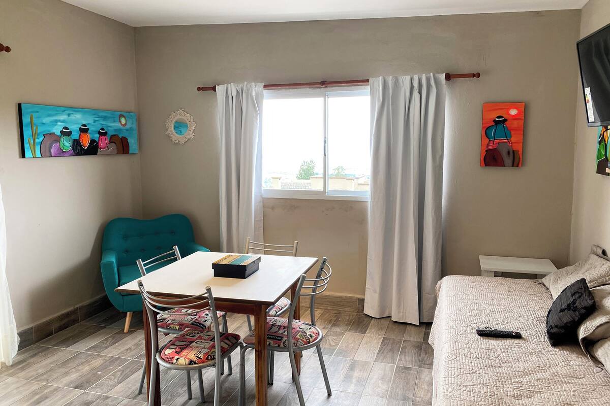 A room with a dining table, chairs, a sofa, a TV, and artwork on the walls.