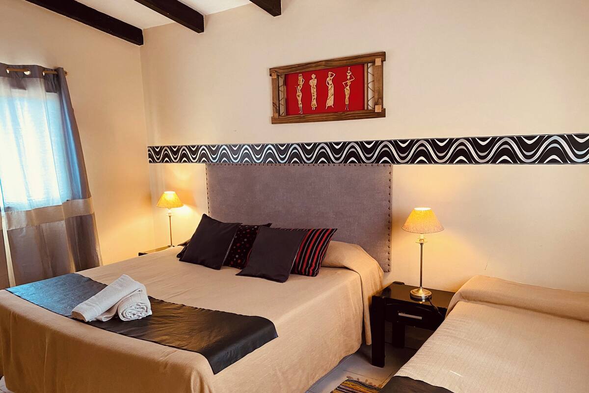 A double bed with a grey headboard, two bedside tables with lamps, a patterned wall, and a framed artwork above the bed.