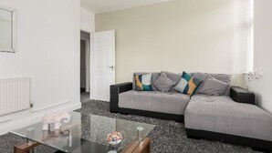 A modern living room with a grey sofa, a glass coffee table, and a white radiator. - Luxury 3 bedroom apartment (Boscombe)