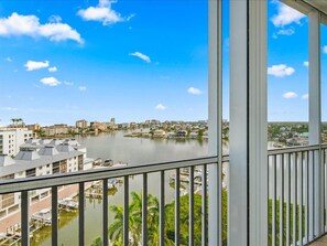 A balcony with a view of a calm river, buildings, and a clear sky. - 10th-Floor Luxury Condo with Stunning Bay &Gulf Views I Walk to Vanderbilt Beach (Naples)