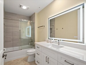 A modern bathroom with a glass shower enclosure, a white vanity with a large mirror, and a toilet. - 10th-Floor Luxury Condo with Stunning Bay &Gulf Views I Walk to Vanderbilt Beach (Naples)