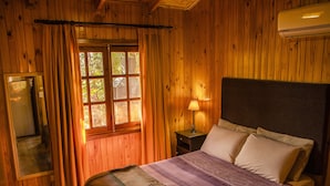 A wooden room with a bed, a nightstand, a lamp, and a window with curtains.